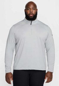 Szürke hosszú ujjú pulóver magas gallérral és félcipzáras záródással. Texturált felülettel és fekete logó díszítéssel az ujjon.