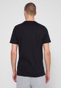 Zwart katoenen T-shirt met korte mouwen, ronde halslijn en een gladde textuur, gezien van achteren, zonder zichtbare afbeeldingen of patronen.