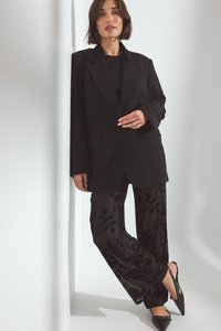 Melns pielāgots bleķis ar strukturētu siluetu, pārī ar caurspīdīgām melnām biksēm ar ziedu rakstu un smailām melnām čībām. Vienkārši aksesuāri.