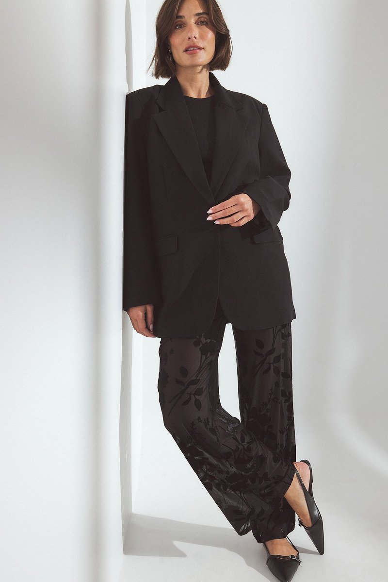 Melns pielāgots bleķis ar strukturētu siluetu, pārī ar caurspīdīgām melnām biksēm ar ziedu rakstu un smailām melnām čībām. Vienkārši aksesuāri.