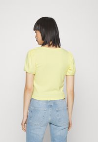 Top amarelo com textura em nervuras, de mangas bufantes, design ajustado e decote redondo, combinado com jeans de ganga azul claro.
