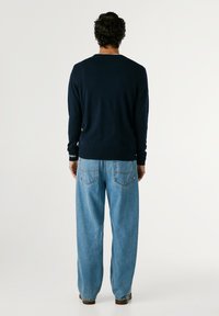 Suéter de manga larga azul marino con puños acanalados, combinado con jeans holgados de color azul claro que cuentan con bolsillos traseros y detalles de costura.