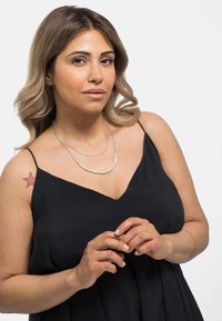 Dubbele ketting met zilveren kettingen en kleine witte kralen. Het onderwerp draagt een zwart mouwloos jurkje, waarop een ster tattoo op de schouder zichtbaar is.