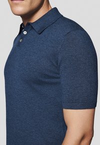 Granatowa koszulka polo wykonana z miękkiego materiału, z kołnierzykiem, krótkimi rękawami oraz zapięciem na trzy guziki. Slim fit z ściśniętymi mankietami.