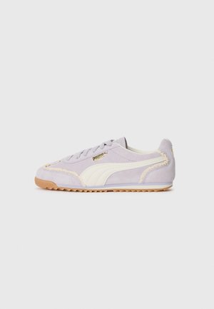 Jasnofioletowy zamszowy sneaker z białym paskiem, beżowym przeszyciem, gumową podeszwą i złotym logo Puma z boku, pokazany z profilu.