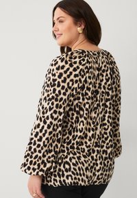 Leopardmønstret bluse med lange ærmer, der har en afslappet pasform, sorte accenter og et blødt, tekstureret stof.