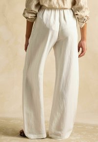 Biele nohavice s širokými nohavicami vyrobené z ľahkej látky s elastickým pásom. Hladká textúra, voľný strih bez viditeľných vreciek.