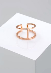 Anello in metallo rosa antico con design aperto, composto da due sezioni curve e una barra verticale centrale; superficie liscia e finitura lucida.