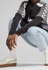 Haut à manches courtes à motif noir et blanc porté sur une chemise à manches longues noire, associé à un jean bleu clair et des baskets blanches avec des semelles marron.