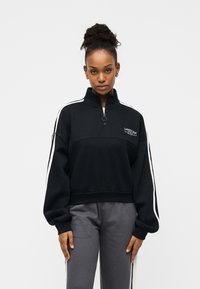 Μαύρο φούτερ με φερμουάρ, λευκές λωρίδες στα πλαϊνά, ριμπ τελείωμα και κεντημένο λογότυπο στο στήθος. Κατασκευασμένο από απαλό ύφασμα, με άνετη εφαρμογή.