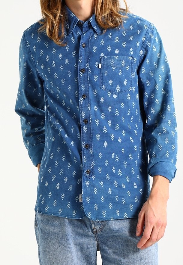 Blauwe spijkerblouse met witte bloemenpatronen, lange mouwen, een knoopsluiting aan de voorkant en een borstzak. Zachte textuur met een ontspannen pasvorm.