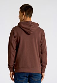 Mörkbrun hoodie med foder i huvan, ribbad mudd och rak nederkant, i kombination med denimjeans med en enfärgad strukturerad tyg.