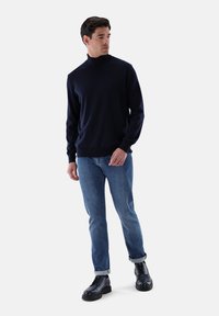 Dunkelblauer Rollkragenpullover, gestrickte Textur, kombiniert mit hellblauen Jeans und schwarzen Leder Schnürstiefeln, hochgerollte Säume an den Jeans.