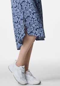 Väljettävä tummansininen mekko, jossa on vaaleansinisiä kukkakuoseja ja sivuhalkioita. Yhdistettynä valkoisiin urheilukenkiin.