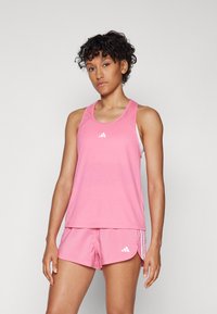 Roosa sportlik tank top valge logoga, koos sobivate roosade lühikesed pükstega, millel on valged külgjaotised. Kanga välimus on kerge ja sile.