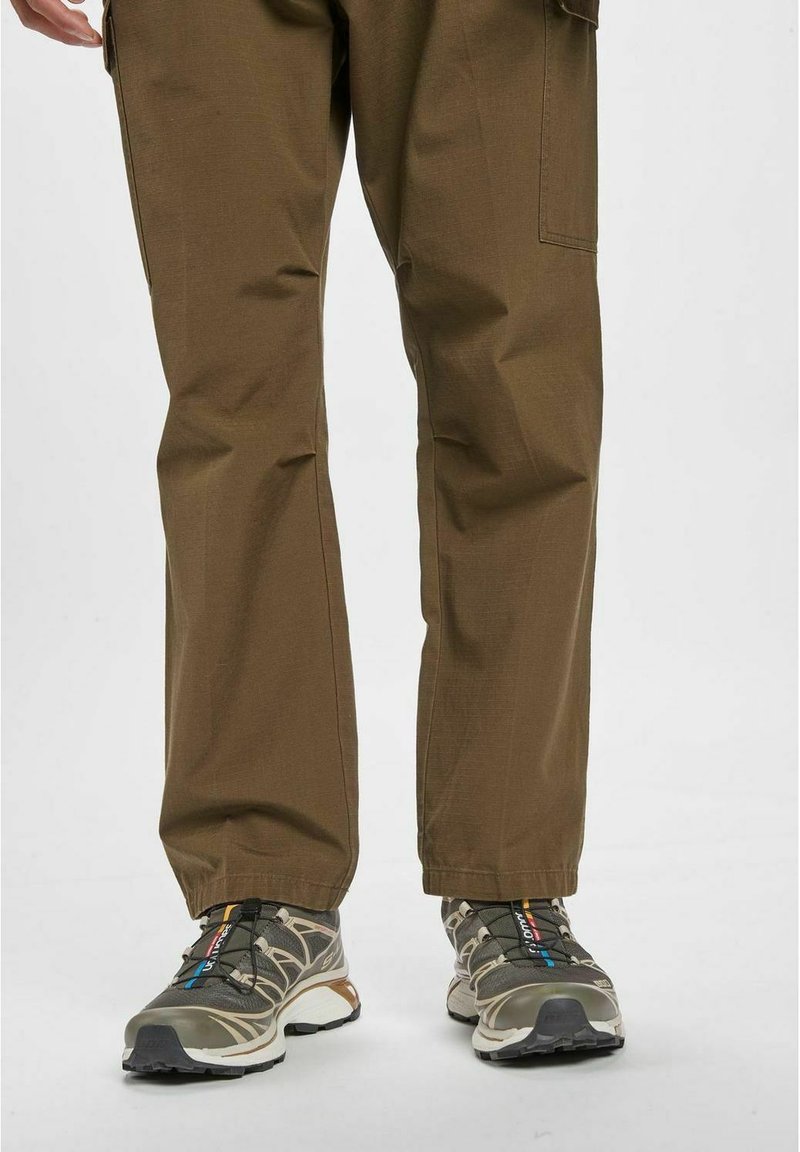 Pantaloni cargo marroni realizzati in tessuto resistente, con una vestibilità comoda e tasche laterali, abbinati a scarpe da ginnastica grigie e blu con lacci.