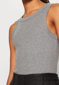 Szary prążkowany top na ramiączkach z okrągłym dekoltem, bez rękawów, o dopasowanym kroju, zestawiony z czarnymi teksturowanymi spodniami.