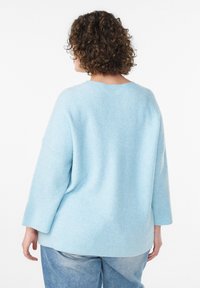 Maglione azzurro chiaro a coste, con vestibilità rilassata e spalle scese, visto da dietro, abbinato a jeans in denim chiaro.