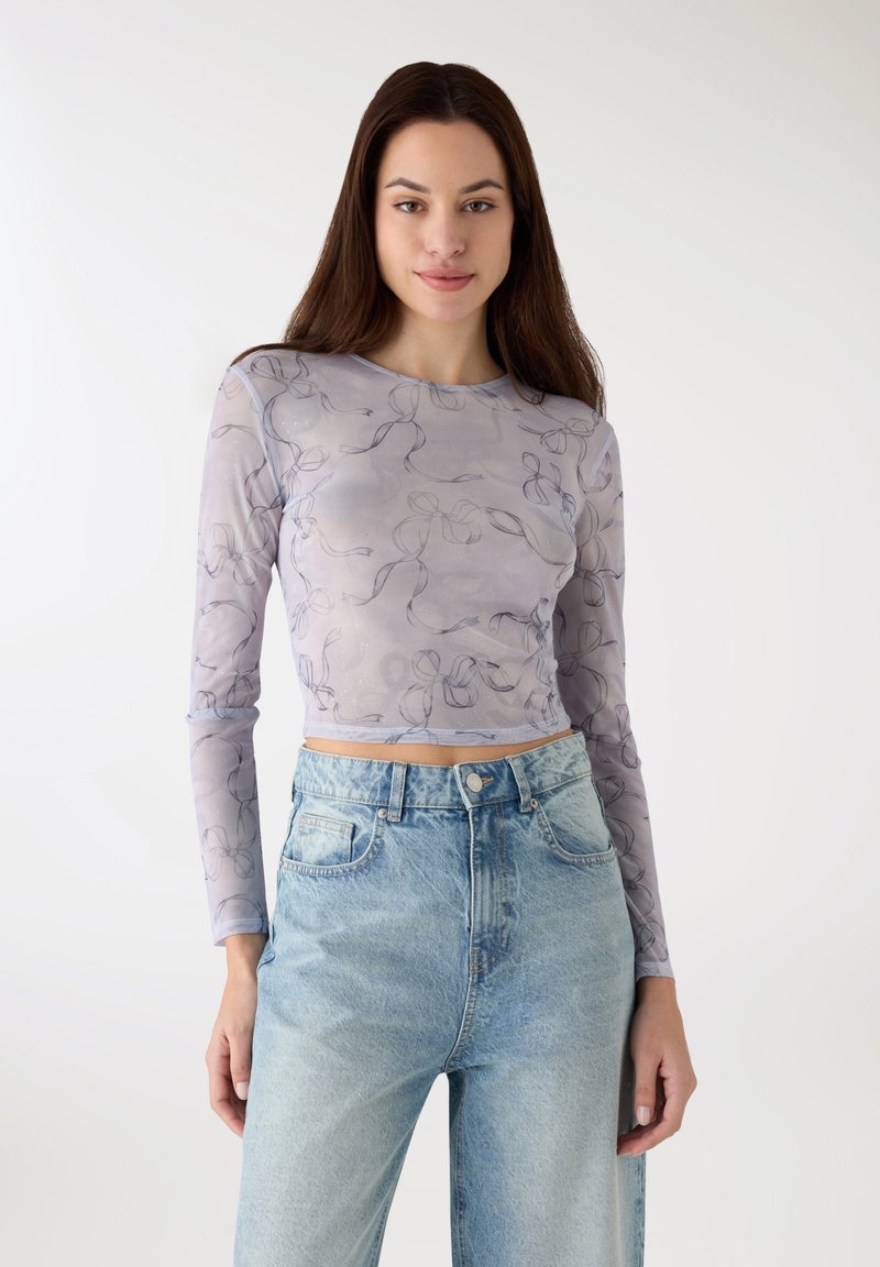 Top corto a maniche lunghe in tessuto viola chiaro trasparente con motivo floreale circolare, abbinato a jeans a vita alta in denim blu slavato.