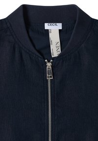 Veste en lin bleu marine avec col côtelé, fermeture éclair métallique et étiquettes blanches indiquant la marque "CECIL" et les détails du tissu à l’intérieur du col.