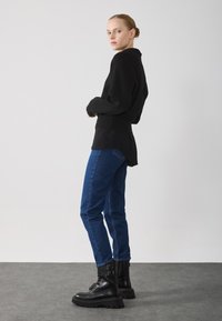 Jersey negro texturizado con dobladillo acanalado, combinado con jeans ajustados azules y botas negras gruesas con hebillas laterales. Diseño simple y moderno.