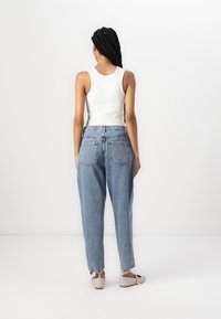 Lyseblå denim high-waisted jeans med afslappet pasform, der har et snævrere ben og to baglommer. Bæres med en hvid tanktop og beige sko.