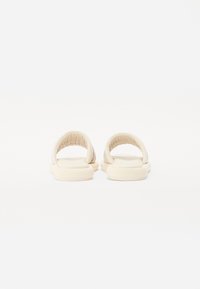 Sandales à glissière beige clair avec des sangles matelassées, un dos ouvert arrondi et une semelle rembourrée, présentant une texture lisse et un design minimaliste.