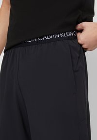 Svarta Calvin Klein-byxor med elastisk midja, slät yta, rak bendesign och sidofickor. Fokus på mångsidighet och komfort.