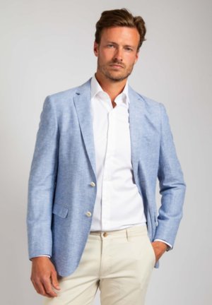 Lichtblauw linnen colbert met twee knopen, notch-revers en zijzakken. Gedragen over een wit overhemd, gecombineerd met beige broek.