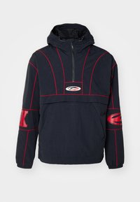 Chaqueta con capucha para hombre en color navy con costuras y acentos rojos. Presenta un cierre frontal de media cremallera, puños elásticos y un gran detalle del logo en el pecho.