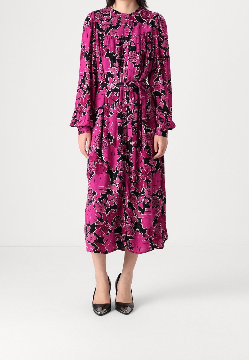 Robe longue rose à fleurs avec des accents noirs. Présente un col haut, des manches longues et une taille ceintrée. Fabriquée en tissu léger.