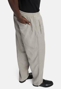 Lichtgrijze broek van een zachte stof, voorzien van een elastische tailleband, zijzakken en een relaxte pasvorm. Gemaakt in combinatie met zwarte schoenen.
