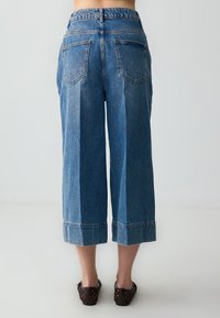 Jean culotte en denim bleu avec une taille haute, des jambes larges et des ourlets repliés. Comprend deux poches arrière et un design classique à cinq poches.