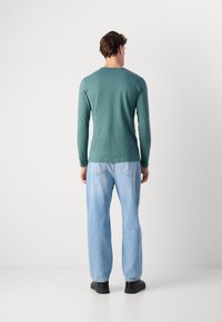Maglietta a maniche lunghe color turchese abbinata a jeans leggeri di un blu pallido e scarpe nere. Design semplice, tessuto di cotone e stile casual.