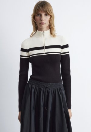 Black and cream striped ribbed sweater with a high neckline and front zipper, paired with a black elastic waistband skirt.