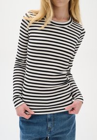 Top a maniche lunghe a righe bianche e nere con scollo rotondo, abbinato a jeans di denim blu. Dettaglio di tessuto testurizzato visibile.