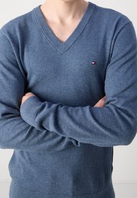 Maglione blu a V in morbido tessuto a maglia, con polsini a coste, vestibilità slim e un piccolo dettaglio del logo sul petto.