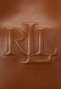 Barna bőr táska, amelyen kidomborított "RL" logó található, sima felülettel és kontrasztos varrással. A dizájn minimalista, további minták nélkül.