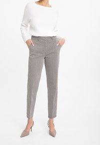 Pull blanc à côtes avec encolure bateau, associé à un pantalon gris à taille haute et à motifs. Le mannequin porte des talons aiguilles taupe.