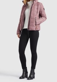 Ljust rosa puffjacka med dragkedja och huva, med ett quiltat mönster och framfickor, i kombination med svarta åtsittande byxor och ankelstövlar.