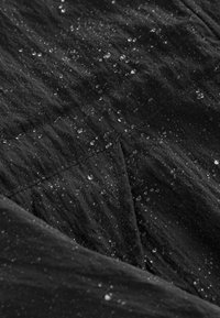 Tissu imperméable noir avec une surface texturée, montrant des gouttes d'eau adhérant à lui, mettant en évidence ses propriétés résistantes à l'eau.