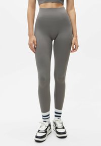 Grijze high-waisted leggings met een gladde textuur. Gecombineerd met gestreepte sokken en zwart-witte sneakers.