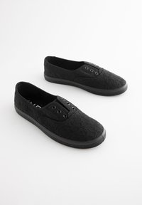 Sorte slip-on sko i blonder med tekstureret overflade, gummisål og dekorative snørehuller foran til snørebånd.