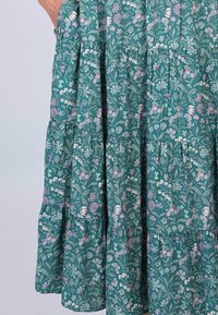 Blumendruckkleid aus türkisfarbenem Stoff, mit gerüschten Volants, kleinen rosa und weißen Blumen sowie grünen Blättern im gesamten Design.