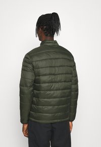 Mörkgrön puffjacka med horisontell sömnad, hög krage och elastiska muddar. Mjuk, slät textur med en lättviktsdesign.