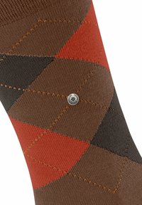 Calzino con un motivo argyle marrone, nero e rosso e un piccolo logo metallico rotondo cucito vicino al centro.