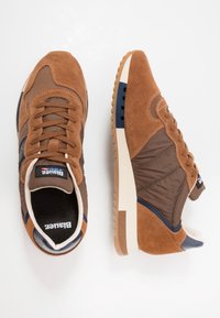 Baskets en daim brun et textile avec une semelle en caoutchouc, présentant un accent marine et des panneaux texturés. Modèle lacé avec un col rembourré.