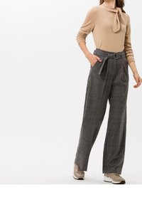 Beiges Sweatshirt mit Bindedetail, kombiniert mit hochgeschnittenen, weit geschnittenen grauen Karohosen. Die Schuhe sind beige Sneakers mit weißer Sohle.