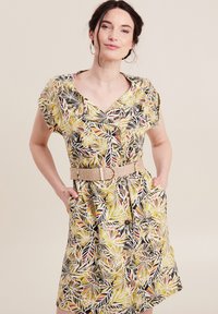 Knopjesjurk in een levendig bladpatroon met gele, zwarte en rode kleuren. Het heeft korte mouwen en een ceintuur in de taille. Inclusief zakken.