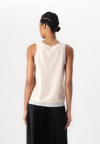 Utenermet bluse i lys beige med en overflate av paljetter og myk stoffkant nederst, kombinert med et svart folderkjole.